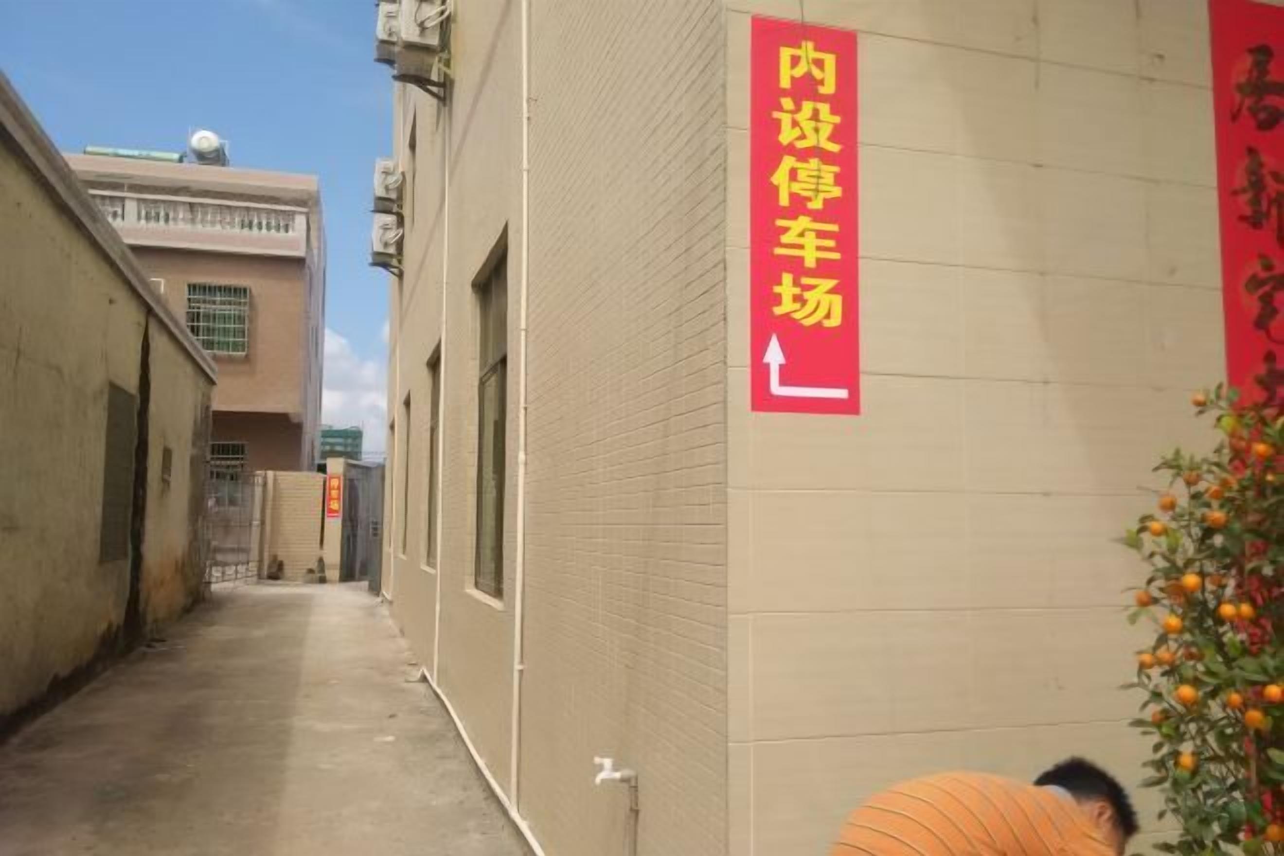 A narrow alleyway with a building on the right side, a red sign with Chinese characters, and a person bending over.