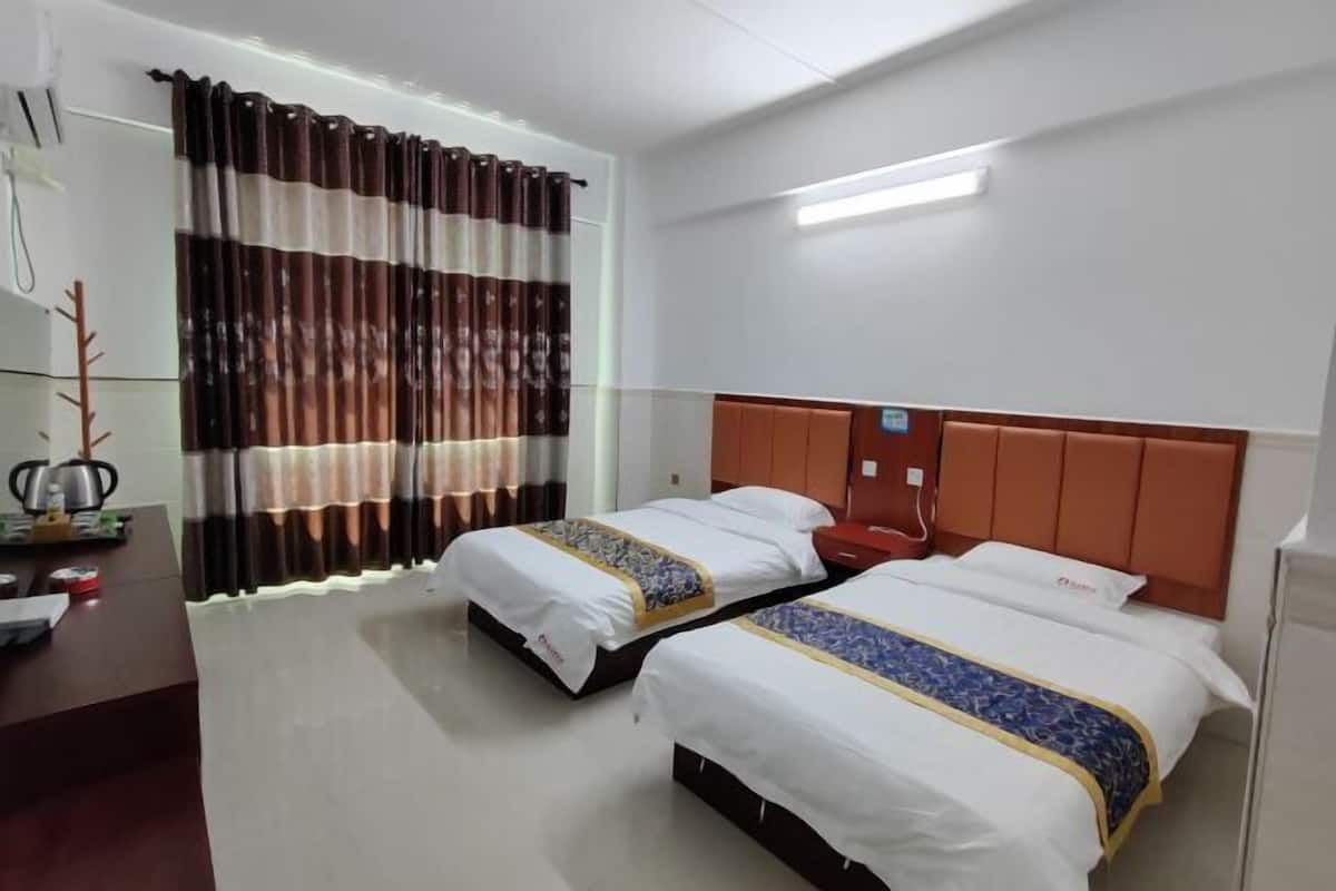 A hotel room with two beds, a desk, and a window with curtains.