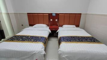 Een hotelkamer met twee enkele bedden, elk met een beddegoed met dessin en witte kussens. Er is een houten hoofdbord, een rode wandtelefoon en een bordje dat de beschikbaarheid van Wi-Fi aangeeft.