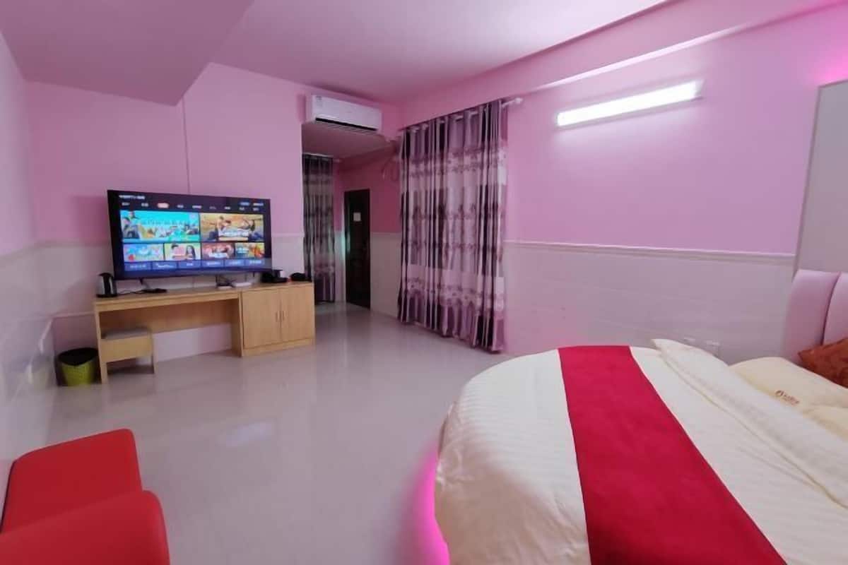 A bedroom with a bed, a desk with a computer, a TV, and a red chair.