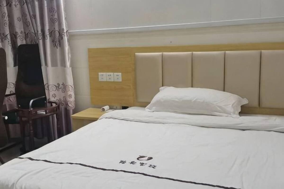 A hotel room with a bed, a chair, a nightstand, and a curtain.
