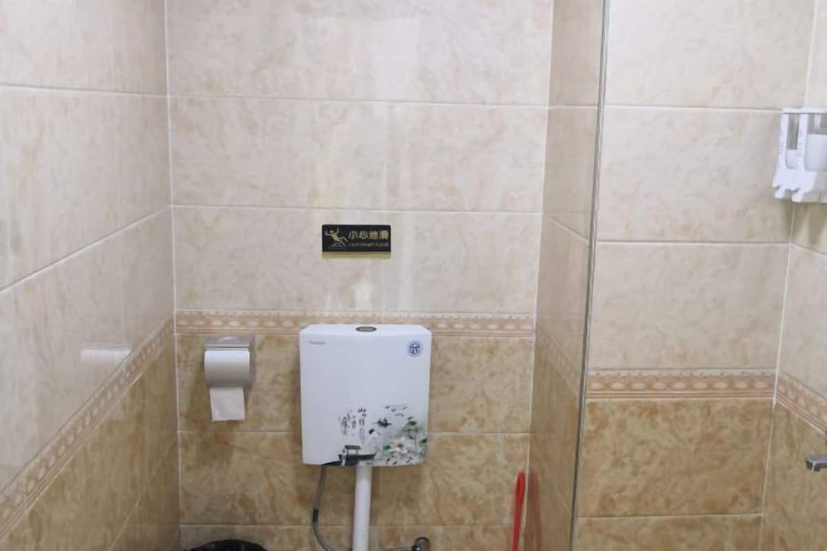 A bathroom with beige tiles, a hand dryer, a paper towel dispenser, and a sign with Chinese characters.