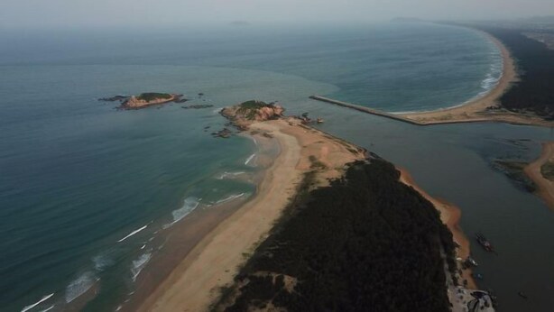 An aerial view of a coastal area with a sandy beach, a small island, and a pier extending into the water. - longzhou hostel (Wanning)