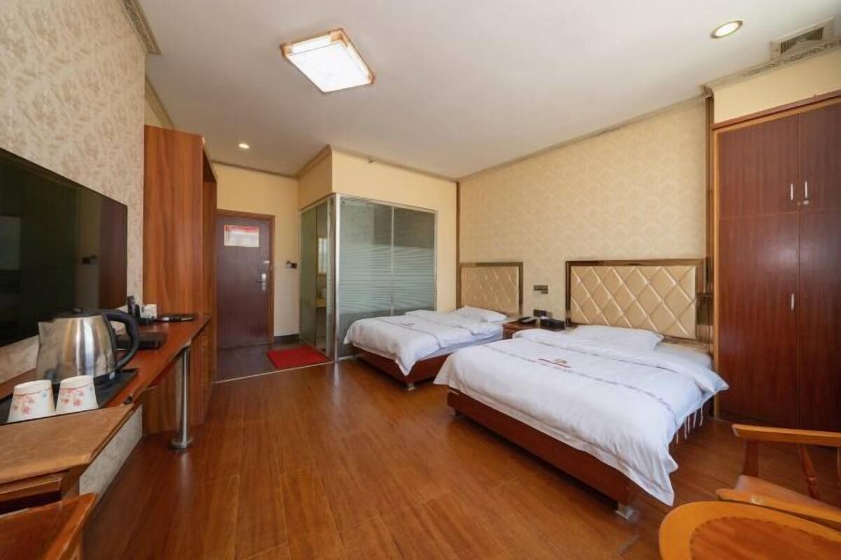 A hotel room with two beds, a TV, a wooden desk with a kettle, and a wardrobe.