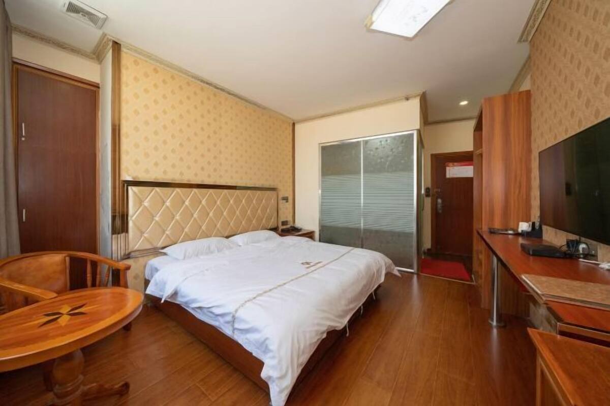 A hotel room with a bed, a wooden chair, a small round table, a TV, and a wardrobe.