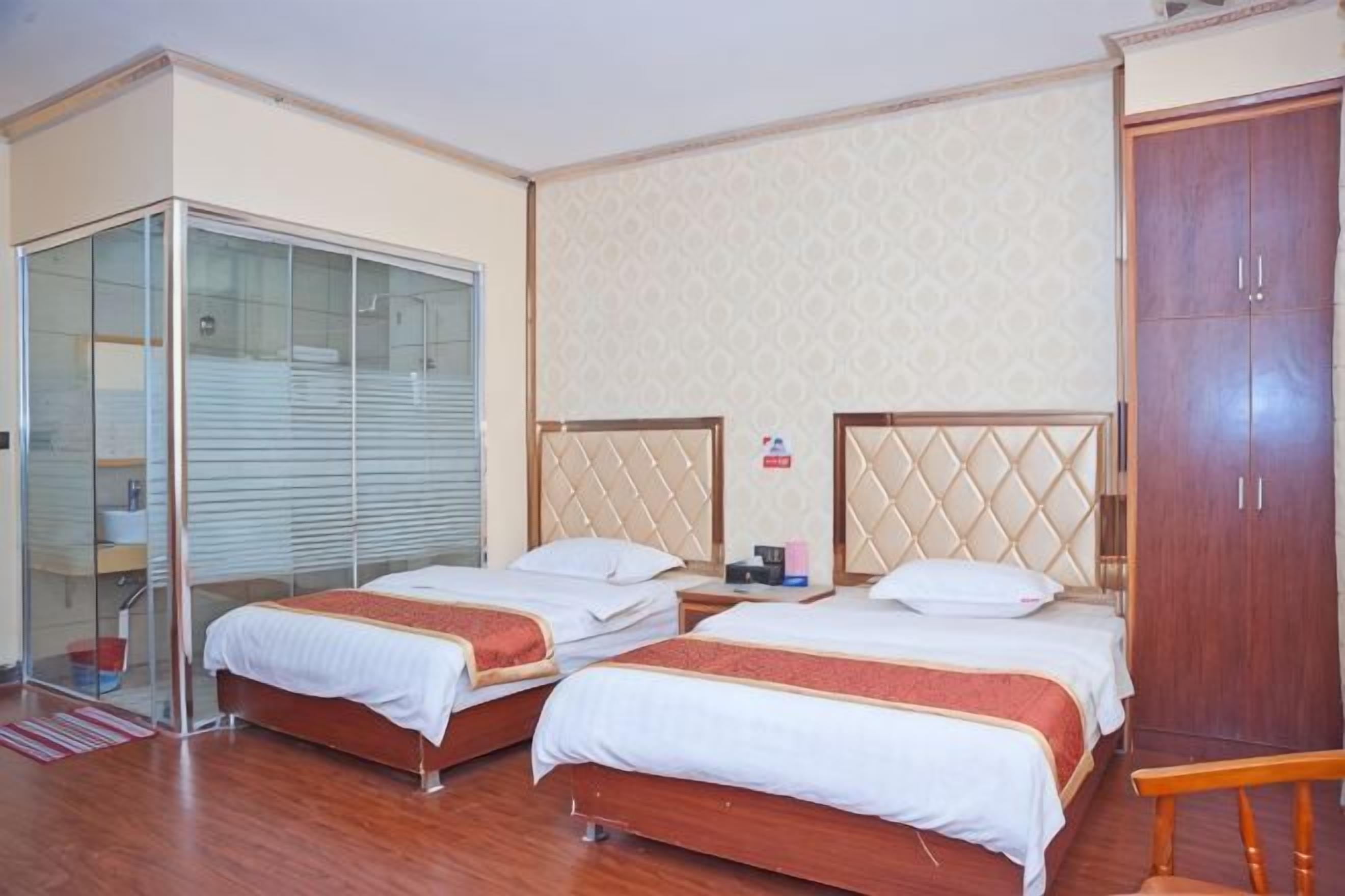 A hotel room with two beds, a wardrobe, and a glass-enclosed closet.