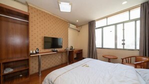 Hotellihuone, jossa on sänky, työpöytä, televisio, tuoli ja ikkuna.