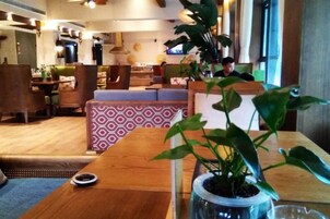 Un vestíbulo de hotel con un mostrador de recepción de madera, zona de estar y una planta grande en maceta.