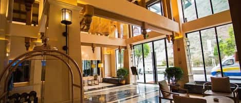A lobby with a grand staircase, a reception desk, and a seating area with tables and chairs.