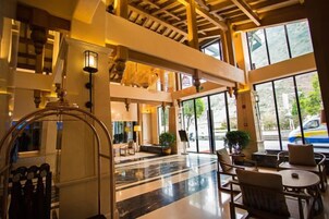 Un vestíbulo con una imponente escalera, una recepción y una zona de estar con mesas y sillas.