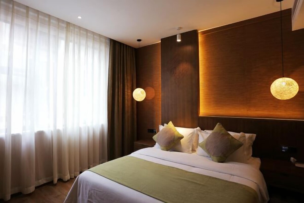Habitación de hotel con cama, cortinas, una lámpara fijada a la pared y un panel de madera.