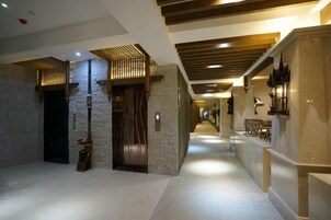 A hotel corridor with a modern design, featuring a stone wall, wooden doors, and a long hallway with a ceiling that has wooden beams.
