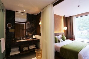 Habitación de hotel moderna con tocador de mármol, cama grande con ropa de cama verde y vistas al exterior a través de un ventanal.