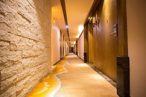Un pasillo con una pared con textura, puertas y un suelo con una sustancia amarillenta.