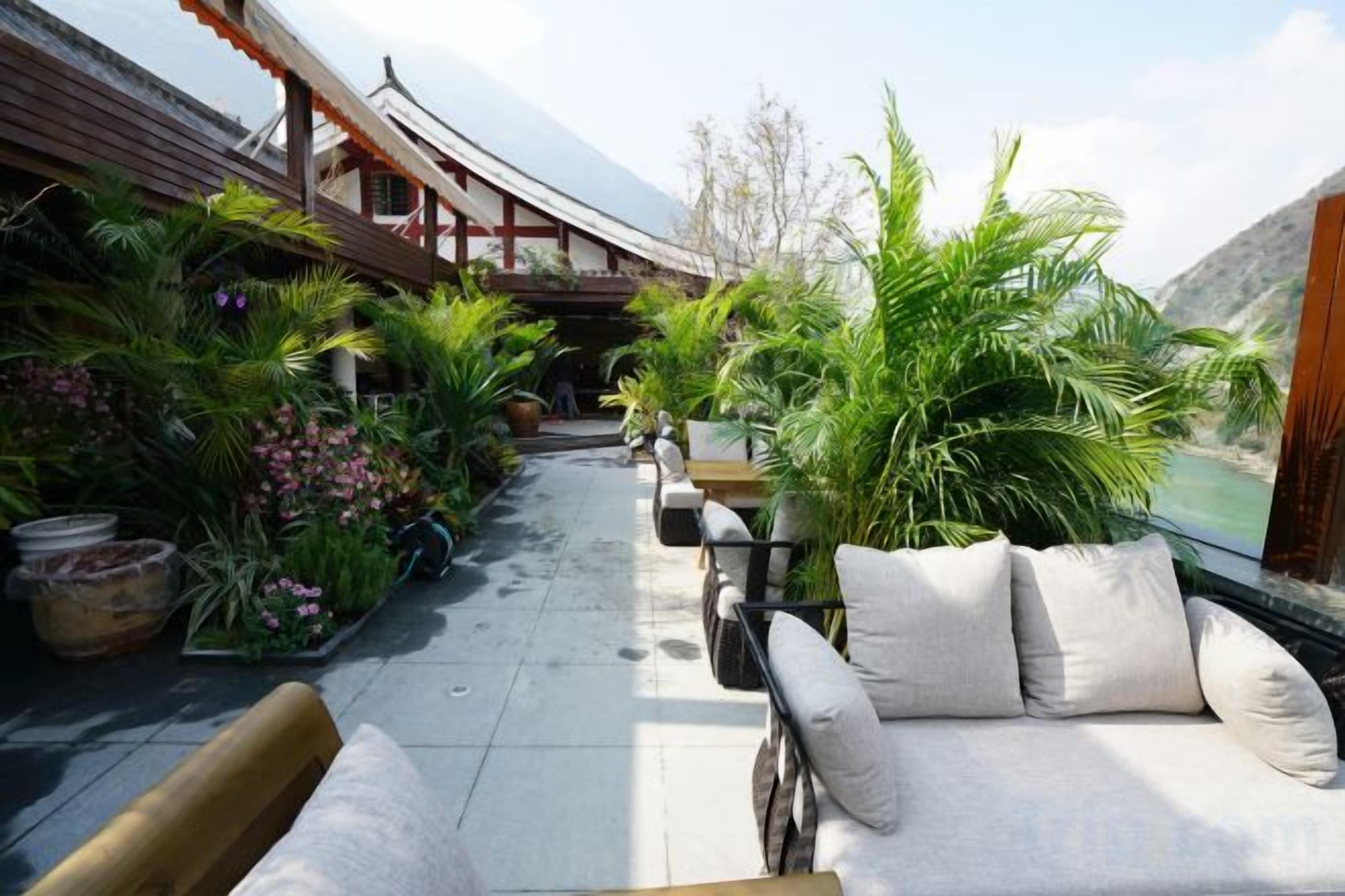Un edificio de estilo tradicional con un corredor cubierto, asientos al aire libre y abundante vegetación.
