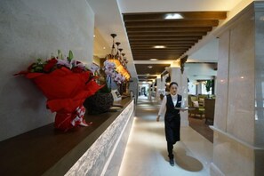 A hotel corridor with a reception area, a large red flower arrangement, and a person walking. - Hong Cheng Hotel (Luding)