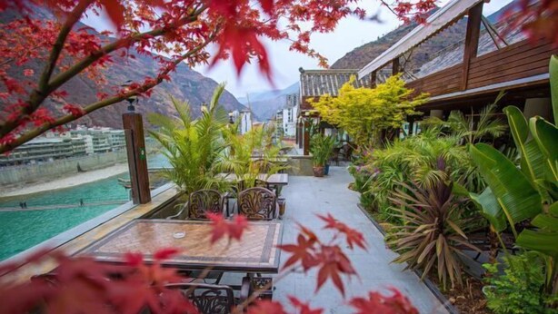 Una terraza con mesa y sillas, rodeada de abundante vegetación y vistas a un paisaje montañoso.