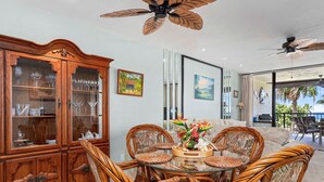 Un comedor con una mesa de vidrio rodeada de sillas de mimbre, un aparador de madera con puertas de vidrio y ventiladores de techo.