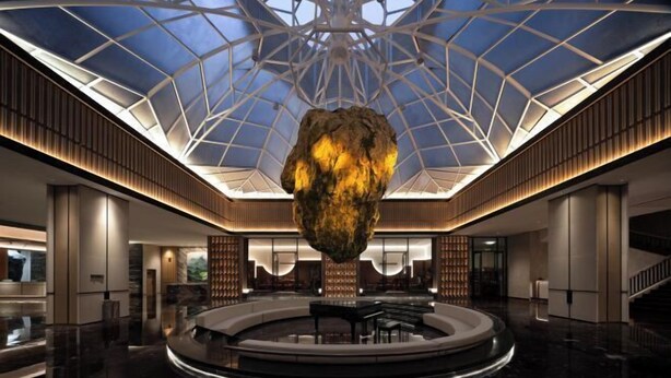 En rummelig lobby med et centralt cirkulært siddeområde, en stor hængende skulptur og et højt loft med et geometrisk glasdesign.