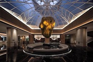 A spacious lobby with a central circular seating area, a large hanging sculpture, and a high ceiling with a geometric glass design. - JP Hyllis Hotel (Lijiang)