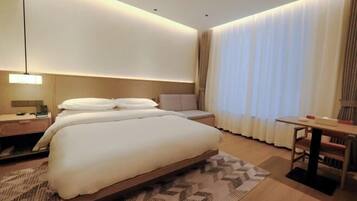 A modern hotel room with a large bed, bedside tables, a desk, and a chair.
