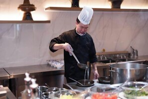 A chef in a professional kitchen with stainless steel appliances and cookware. - JP Hyllis Hotel (Lijiang)