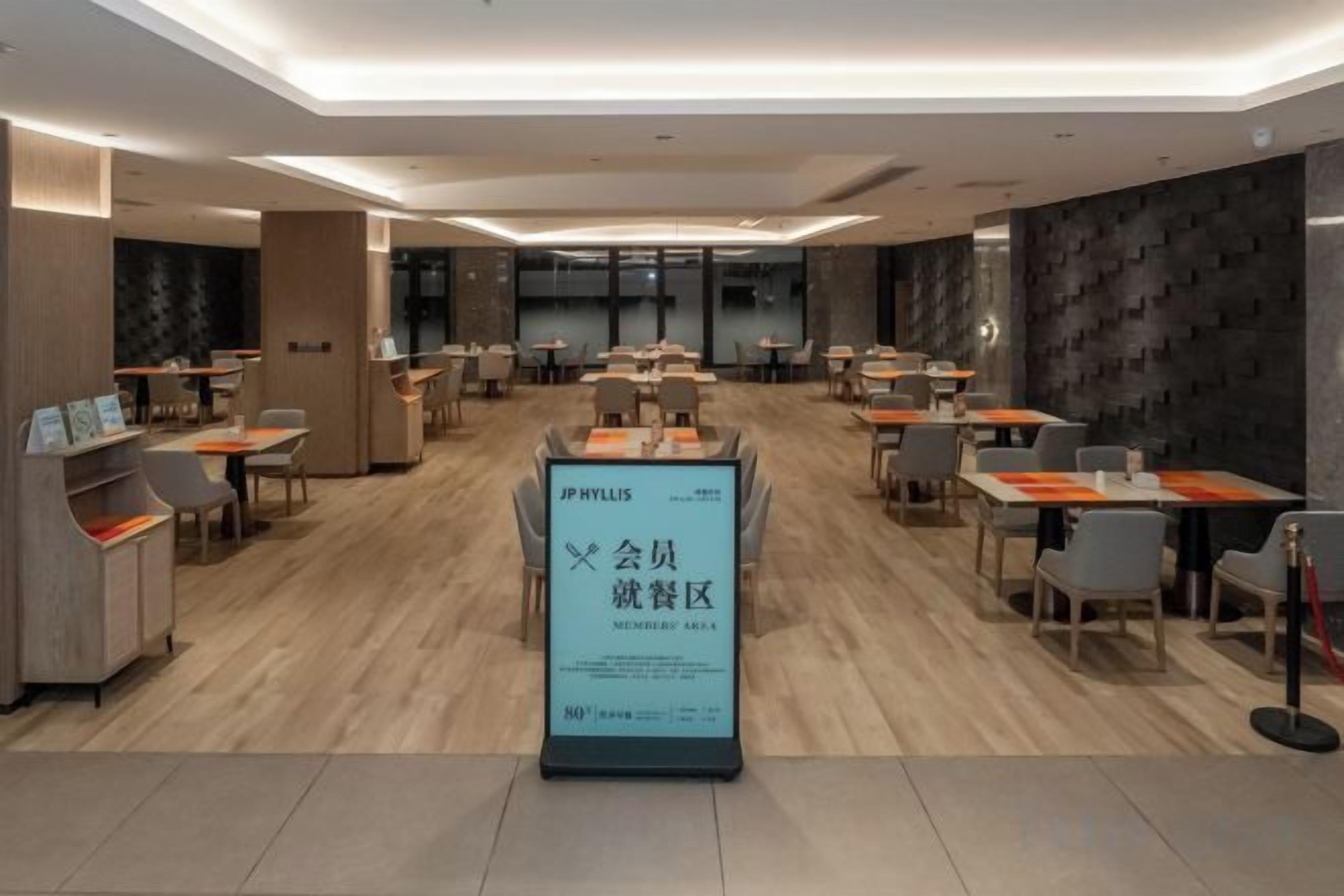 A spacious restaurant with multiple tables and chairs, a central signboard, and a modern interior design.