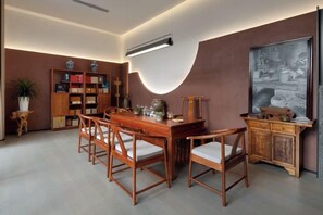 A dining area with a wooden table and chairs, a bookshelf, and a large framed picture on the wall. - JP Hyllis Hotel (Lijiang)