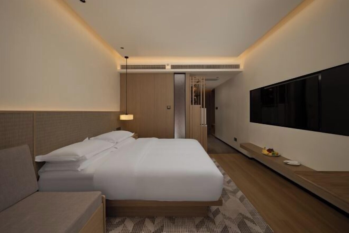 Una habitación de hotel moderna con una cama grande, un televisor y un escritorio pequeño.