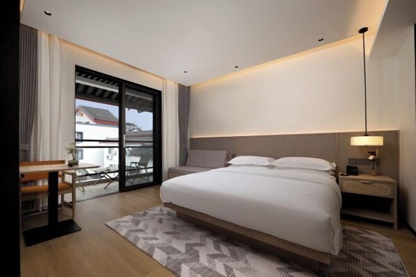 Una habitación de hotel moderna con una cama grande, un escritorio y un balcón con vistas a edificios.