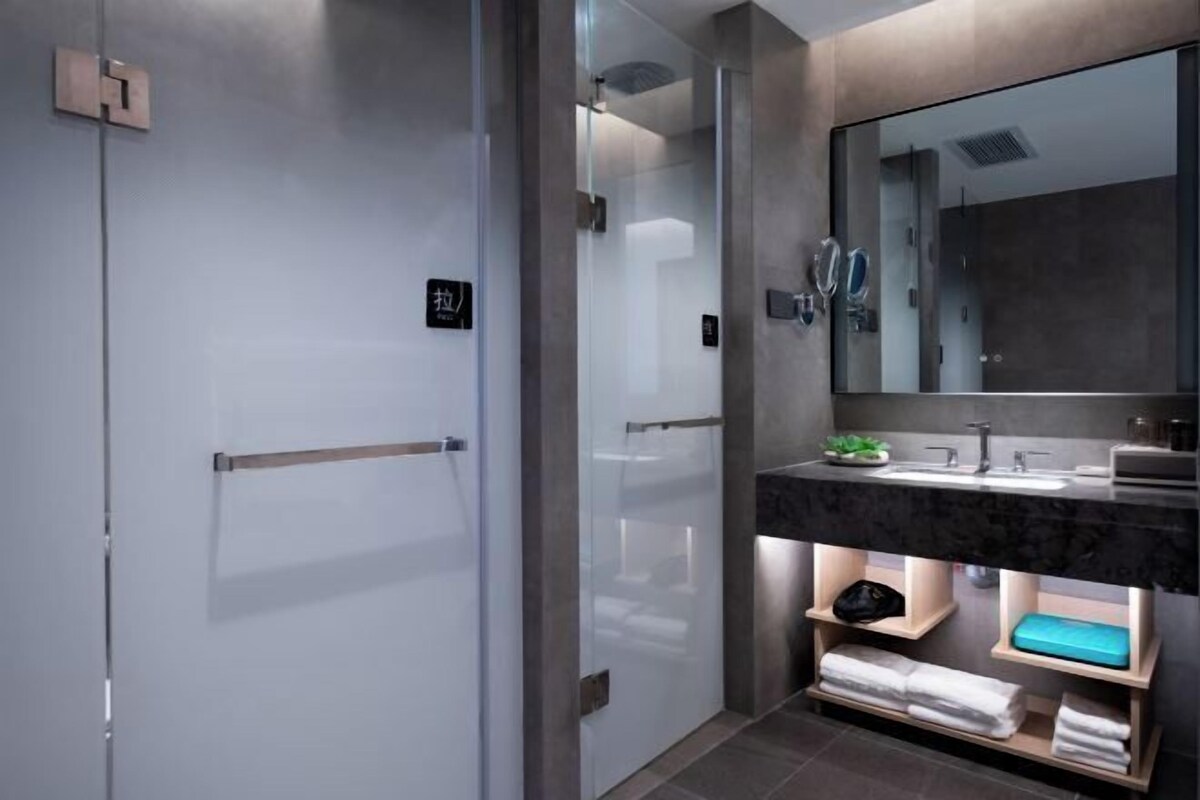 Un baño moderno con cabina de ducha de vidrio, un espejo grande y una encimera de mármol con lavamanos.