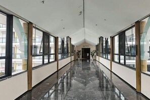 A long, narrow hallway with large windows on both sides, leading to a door at the end. - JP Hyllis Hotel (Lijiang)