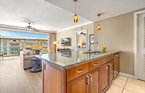 A modern kitchen with a large island, a dining area with a sofa and table, and a balcony with a view of other buildings.