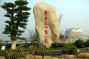 A large rock with Chinese characters, a pine tree, and a building in the background.