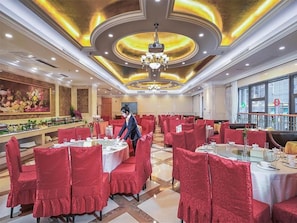 Un restaurante con sillas tapizadas en rojo, manteles blancos y un candelabro.