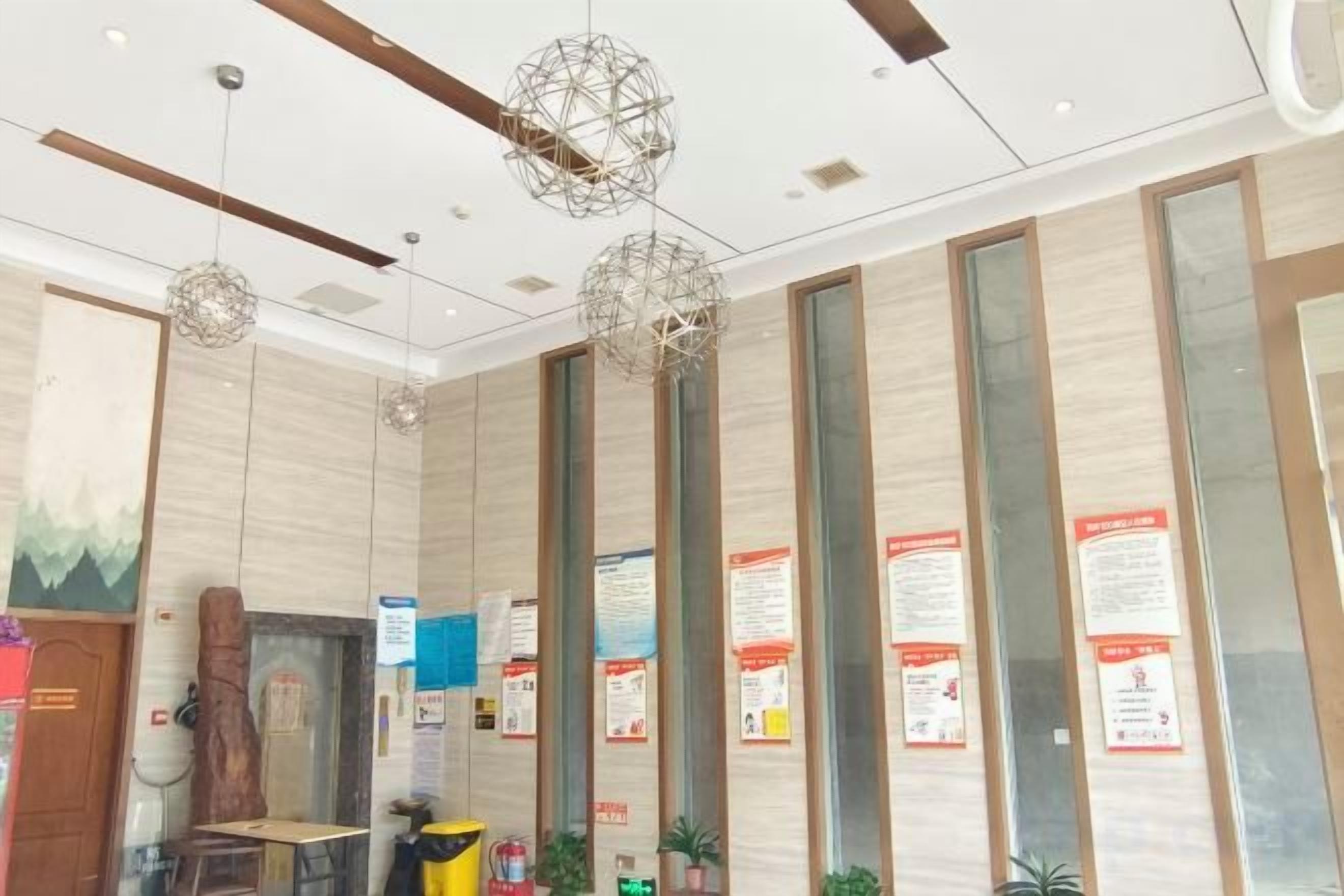 Un espace d’accueil doté d’un comptoir de réception en bois, de luminaires sphériques suspendus, de panneaux de verre verticaux et d’affiches d’information.