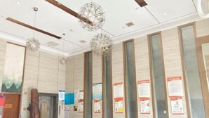 Un moderno vestíbulo de hotel con techo de madera, ventanas amplias y carteles informativos en las paredes.