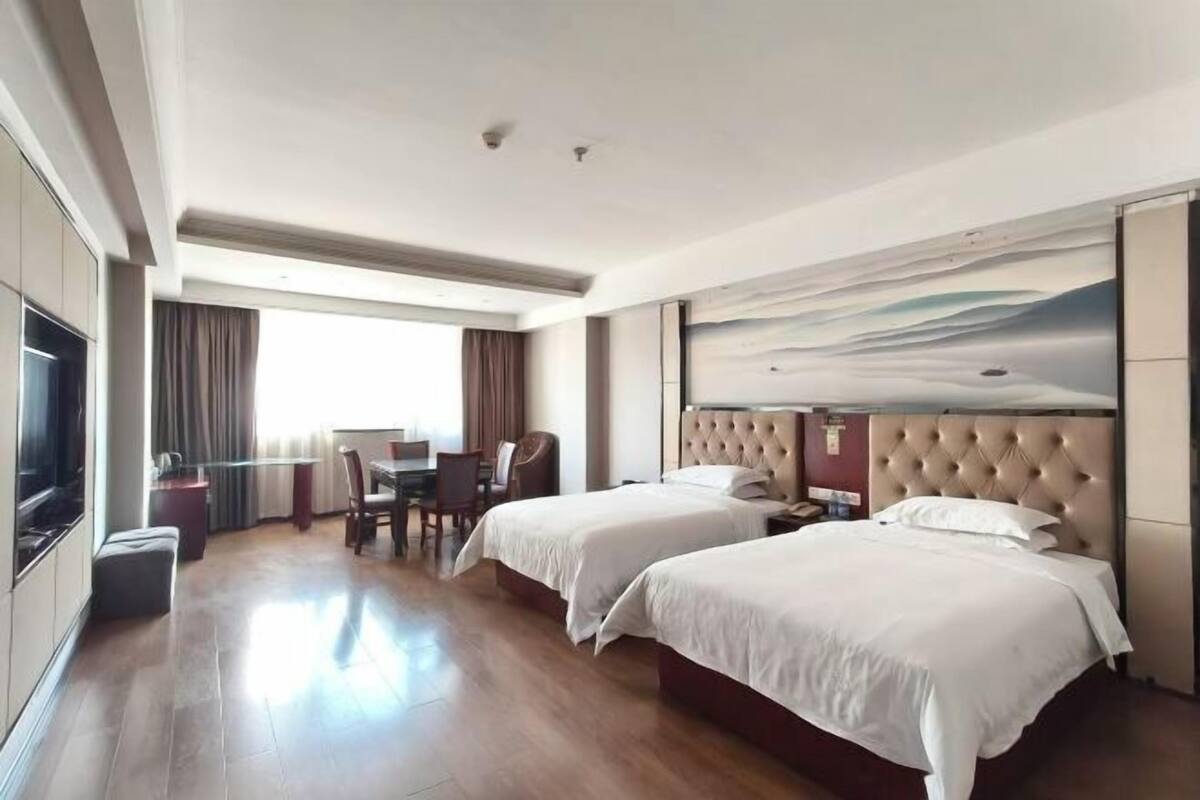 Een hotelkamer met twee bedden, een bureau, een stoel, een televisie en een groot raam.