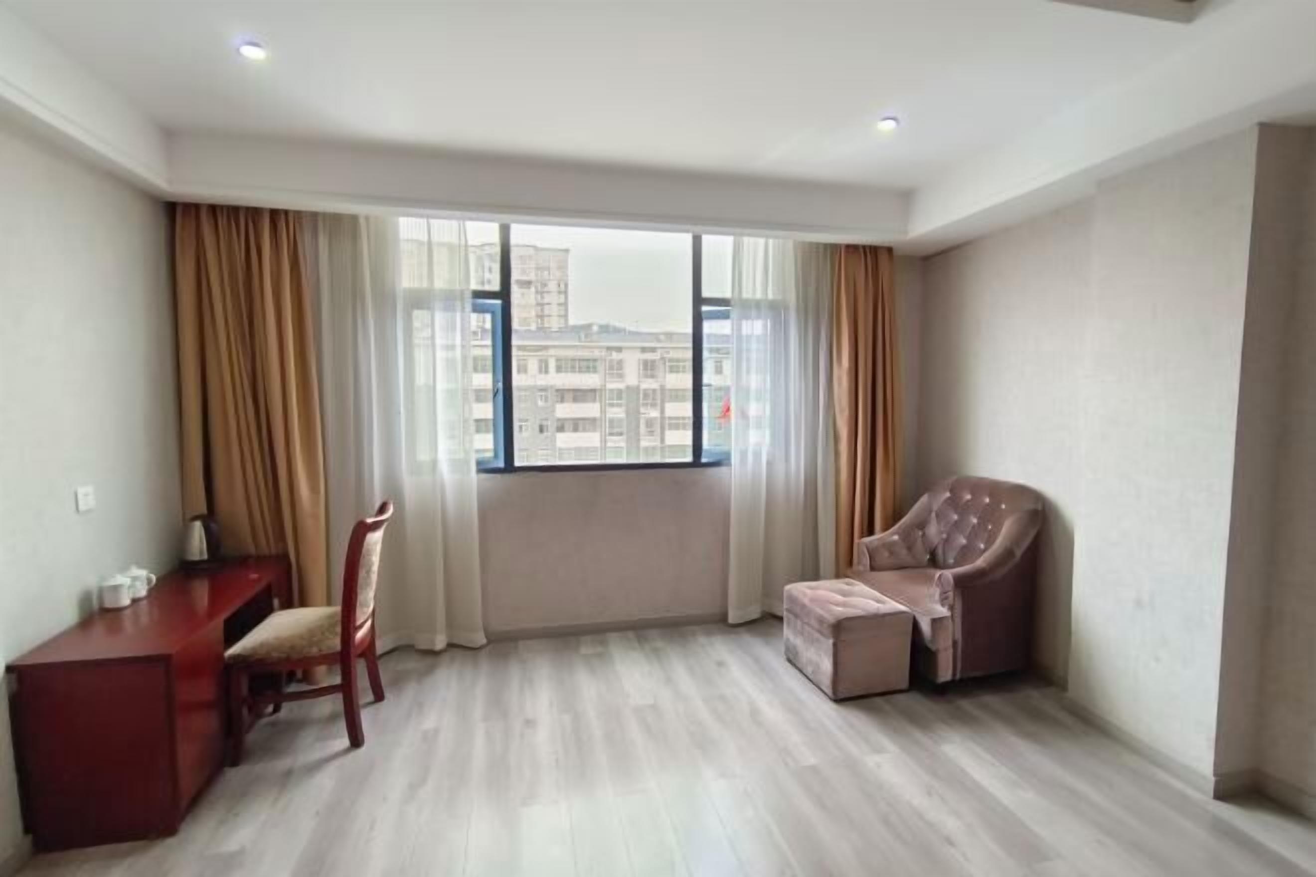 A room with a large window, a desk, a chair, and a sofa.