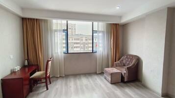 A room with a large window, a desk, a chair, and a sofa.