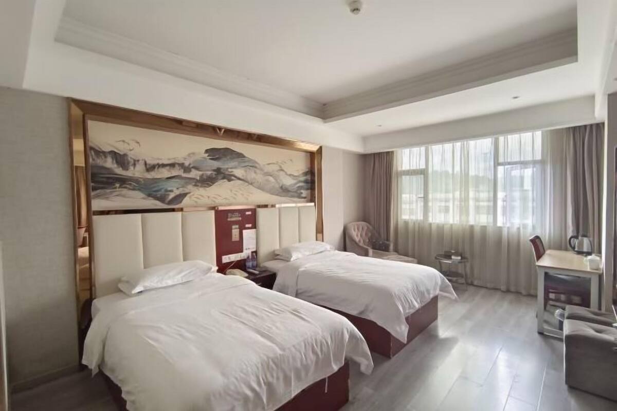 Een hotelkamer met twee bedden, een bureau, een stoel en een groot schilderij aan de muur.