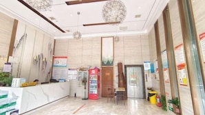 Un vestíbulo de hotel con una recepción, una máquina expendedora, una pequeña mesa con sillas y una puerta de madera.
