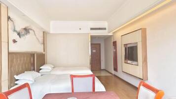 A hotel room with a bed, a table with chairs, a TV mounted on the wall, and a door leading to another room.