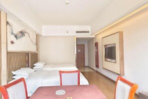 A hotel room with a bed, a table with chairs, a TV mounted on the wall, and a door leading to another room.