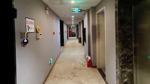 Un pasillo de hotel con piso alfombrado, un detector de incendios, una señal de salida y una puerta a la derecha.