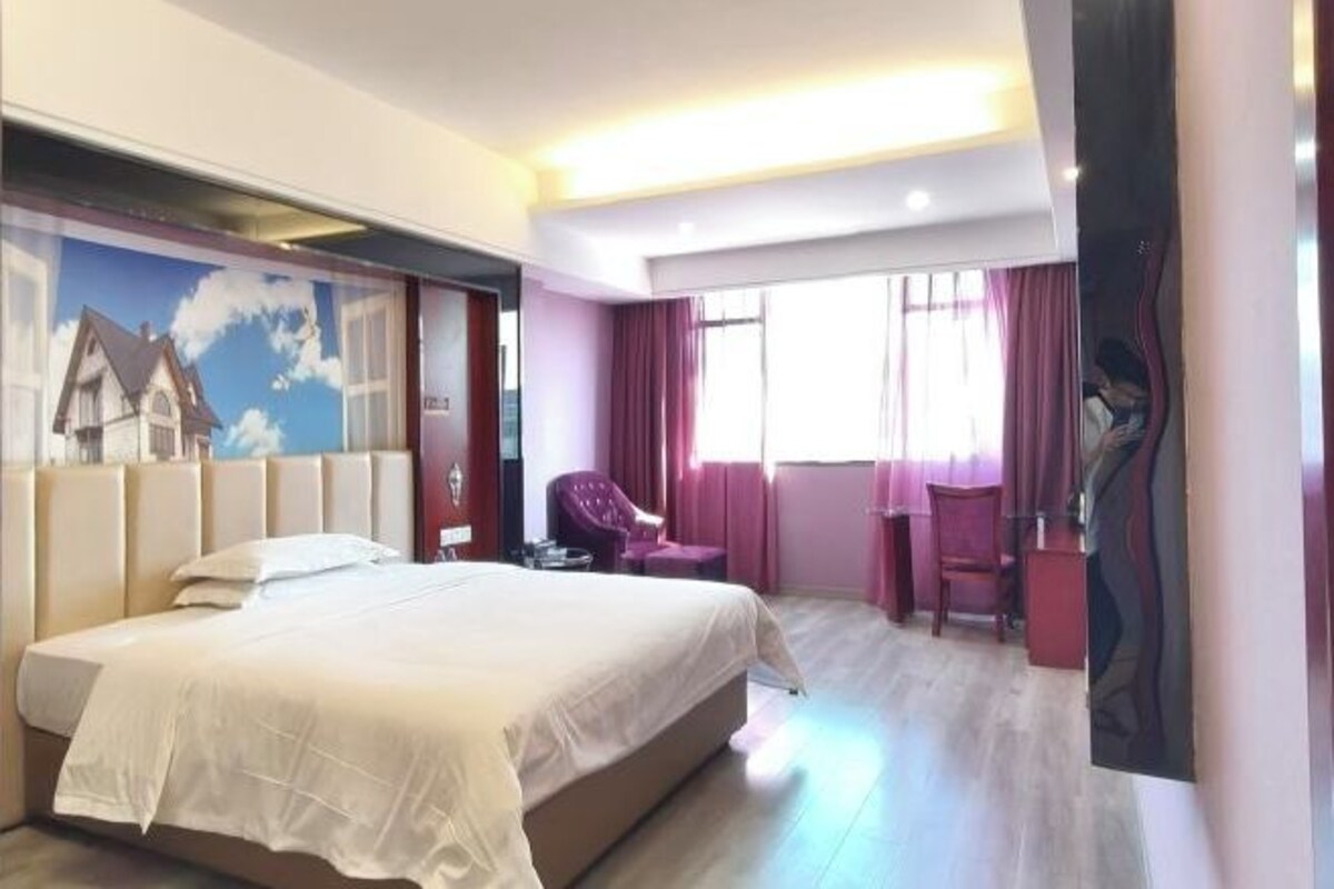Ein Hotelzimmer mit einem großen Bett, einem Sessel, einem Schreibtisch und einem Fenster mit Vorhängen.