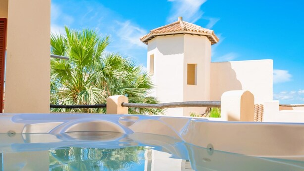 Piscina cristalina que refleja palmeras y un edificio con techo de tejas.