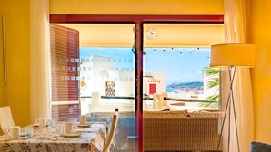 Un comedor con una mesa dispuesta para dos, un sofá de mimbre y vistas de la ciudad a través de una puerta de cristal.