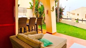 Una habitación con sofá, sillas y un comedor con vistas a un césped verde y un edificio blanco.