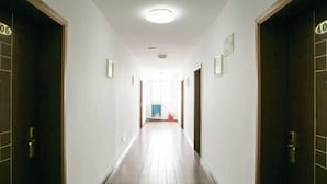 A long, narrow hotel corridor with wooden doors on either side, numbered signs above each door, and a bright ceiling light. - Shaoxing Mingdu Business Hotel (Shaoxing)